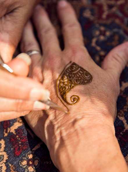 Close das mãos de uma pessoa fazendo tatuagem de henna nas mãos de outra pessoa.