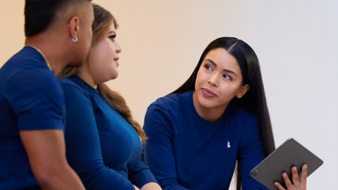 Una empleada de Apple Retail sujeta un iPad mientras habla con dos personas del equipo.