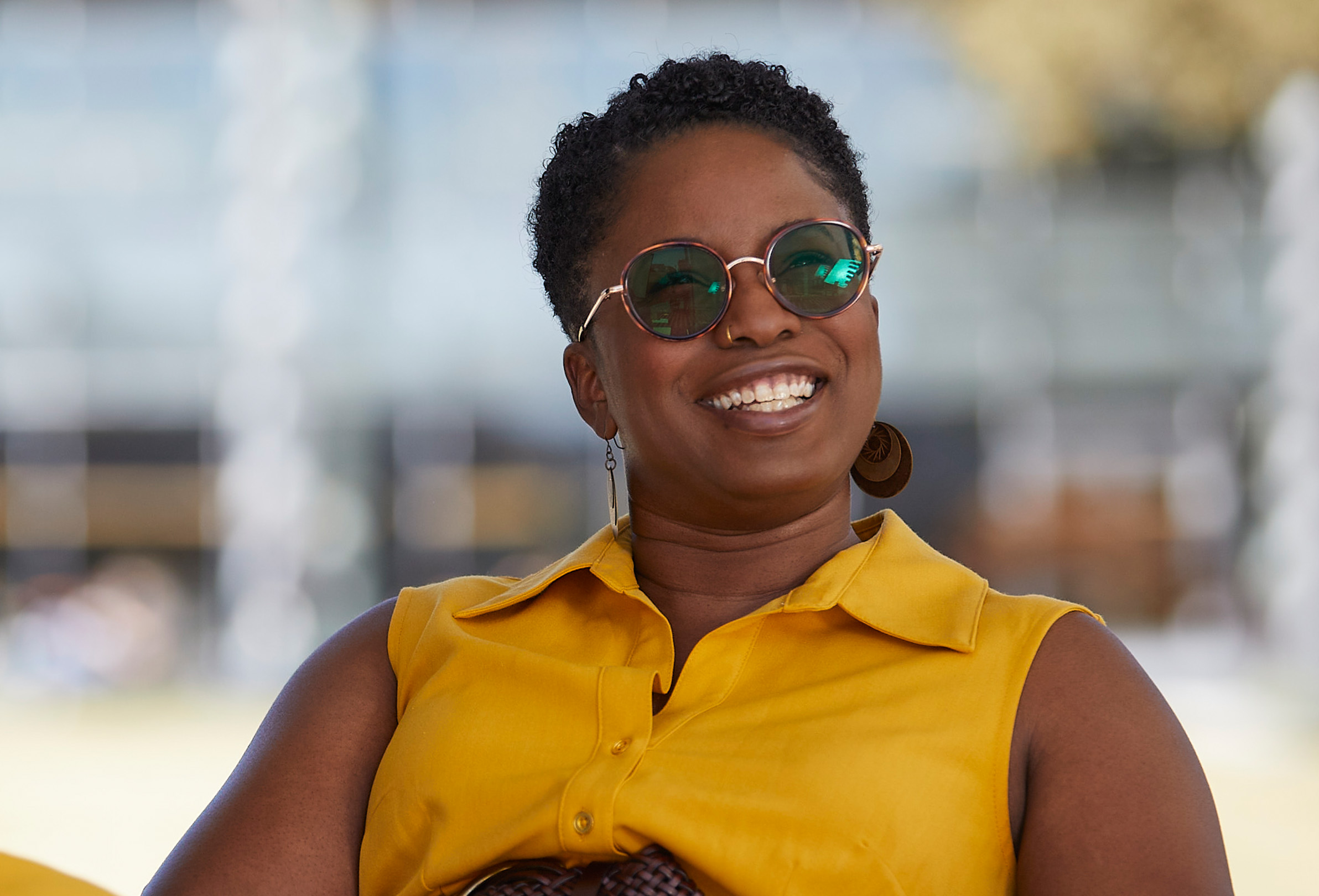 Una empleada de Apple con gafas de sol sonríe sentada al aire libre.