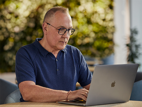 Apple 软件与服务团队的一名员工在户外使用 MacBook，背景是绿色植物。