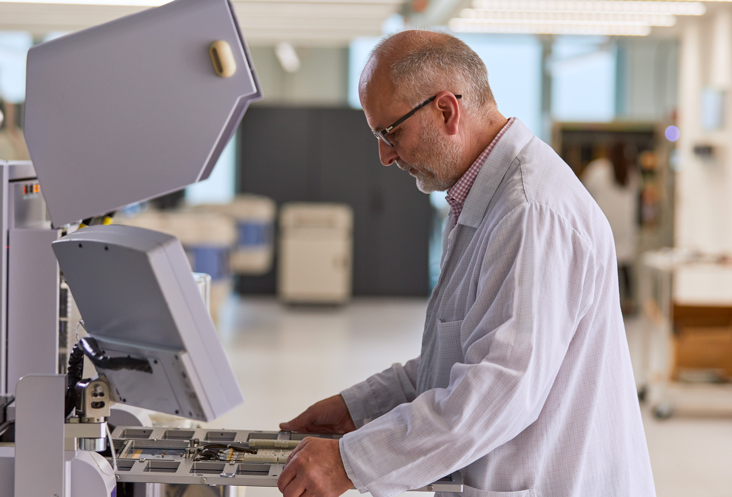 Pracownik Apple w białym fartuchu laboratoryjnym, który zajmuje się sprzętem inżynieryjnym. 