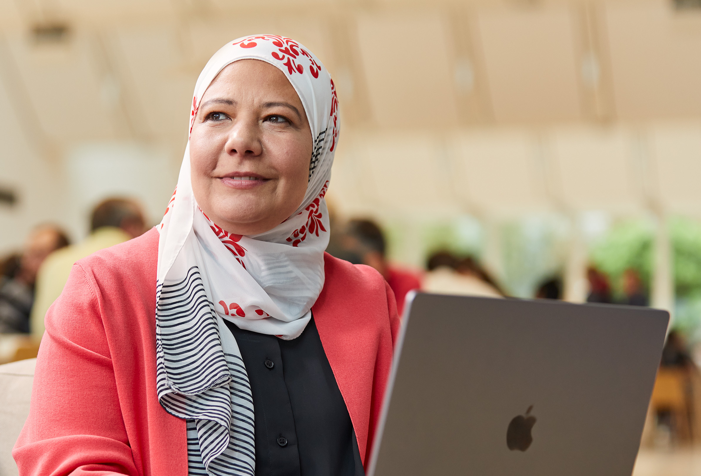 Una empleada de Apple sentada en una mesa con un MacBook y mirando hacia la izquierda.