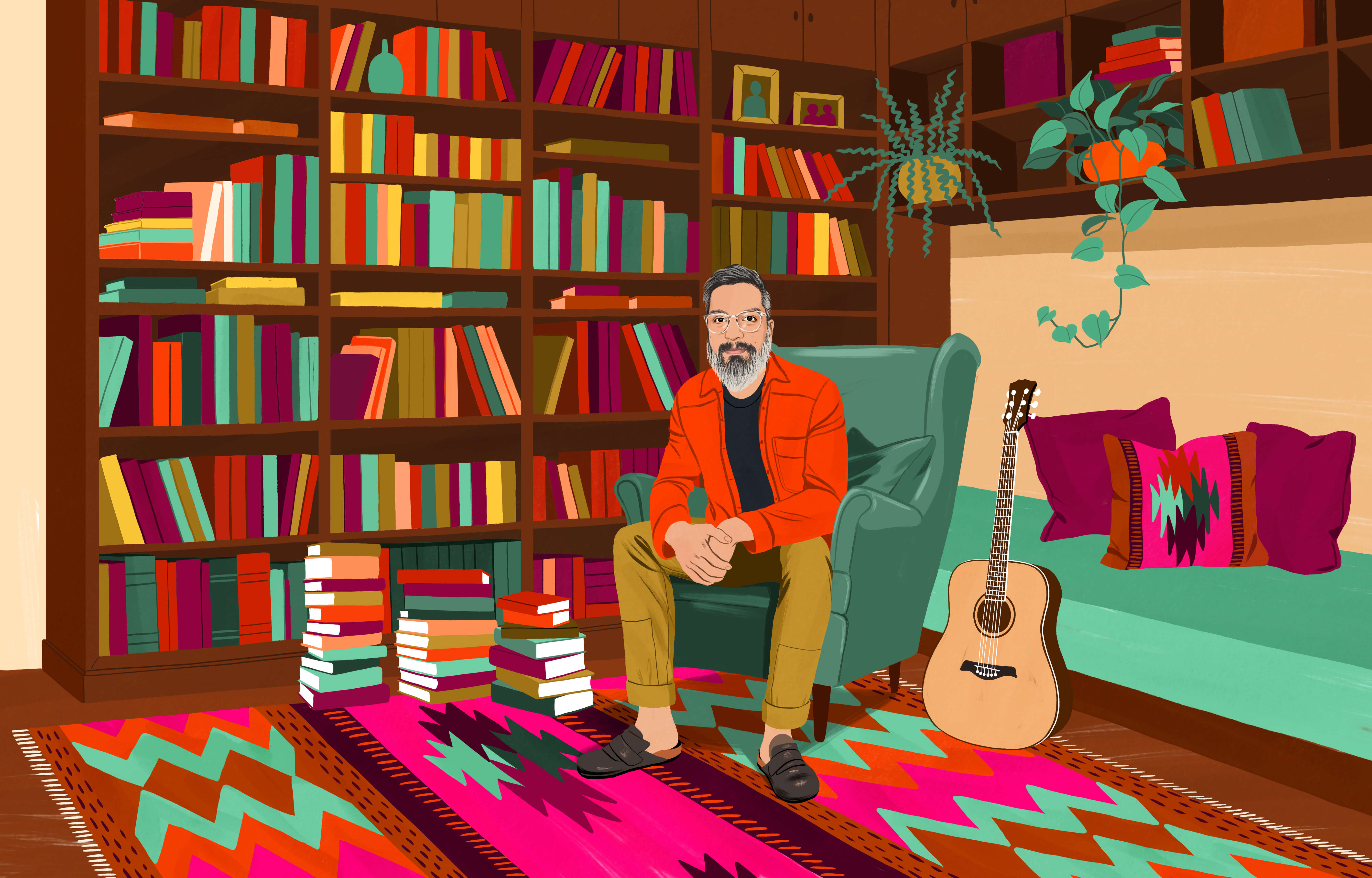 JP sentado en un sillón individual rodeado de un librero repleto de libros y algunos apilados en el suelo. En el piso hay un tapete chileno con un colorido diseño. A su lado hay una guitarra acústica.