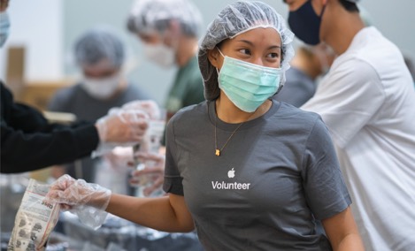 En Apple-praktikant med en volontärtröja från Apple tittar leende åt sidan medan hen packar artiklar vid ett volontärevent.